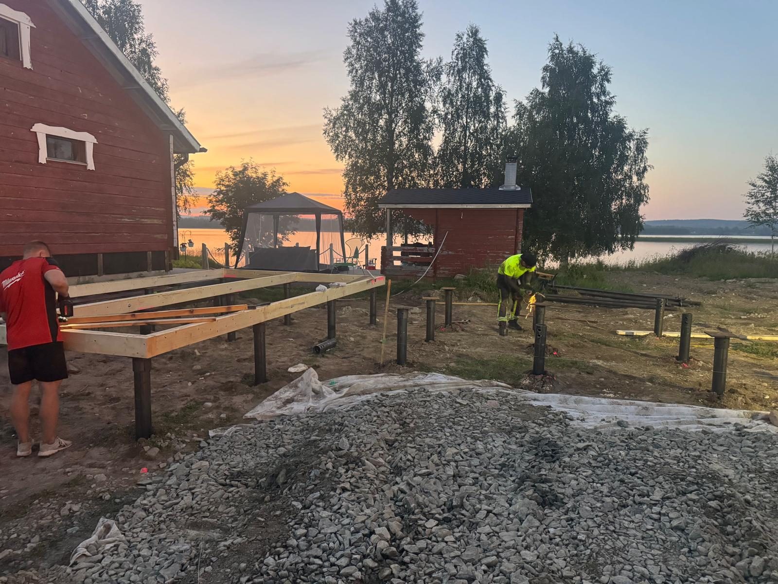 Treballadors construint una estructura de fusta sobre fonamentacions de pilots helicoïdals a la vora del llac